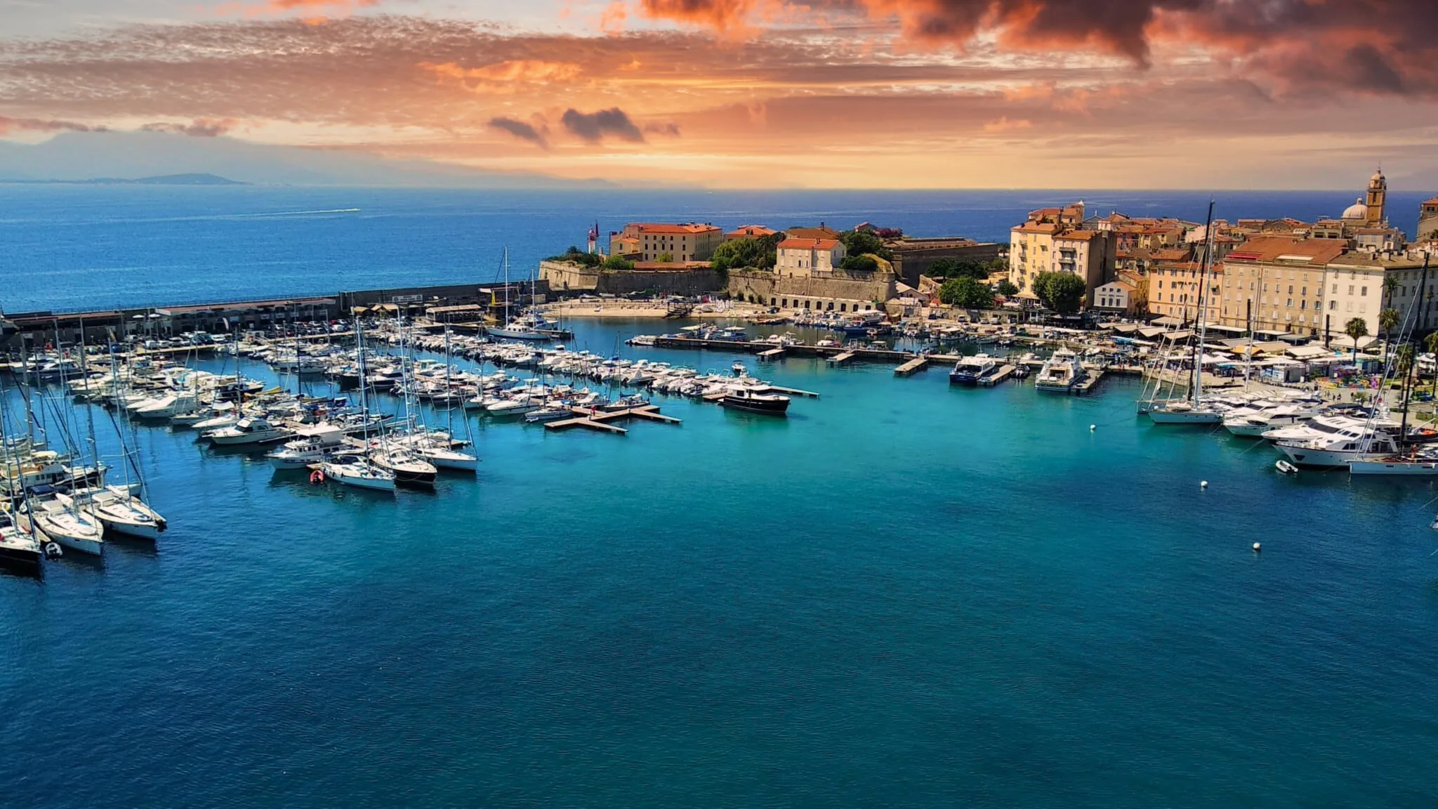 Overhead view of the coastline. Ajaccio, Corsica Marina, with many yachts, blue water and a beautiful orange, cloudy sunset sky.